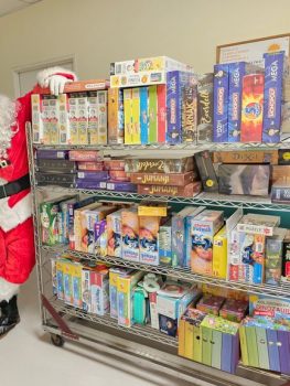 Santa Claus standing next to shelves full of toys and board games donated during Matex Transport Christmas charity event